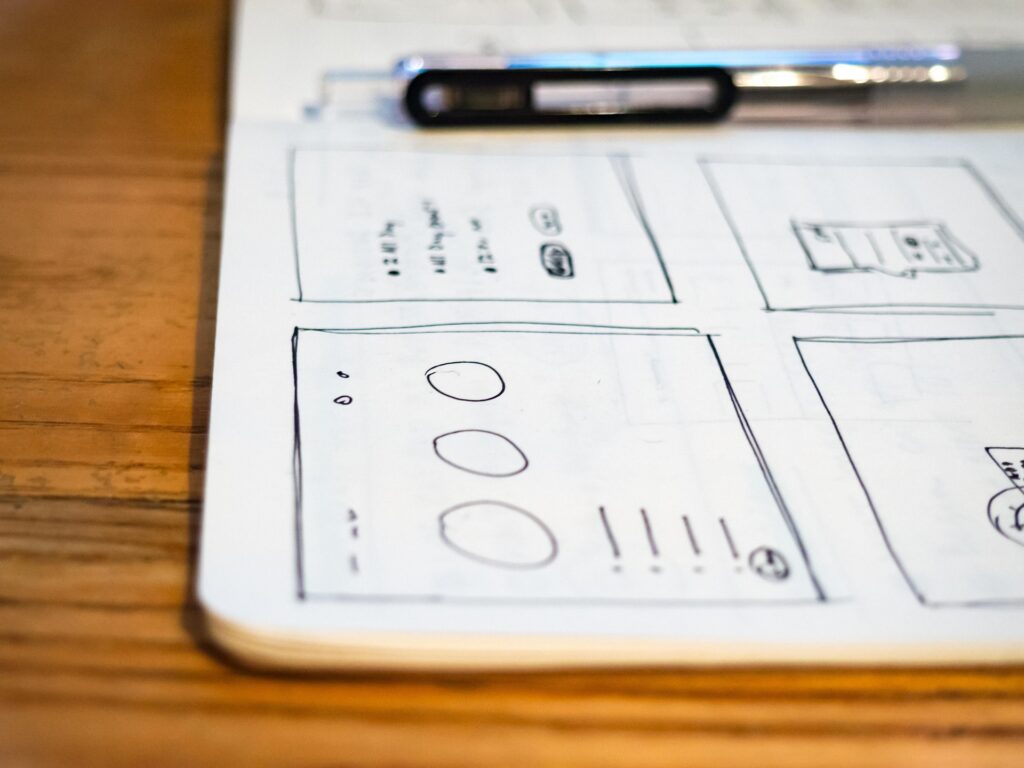Sketches of a layout on paper, drawn with a ballpoint pen on a wooden table.